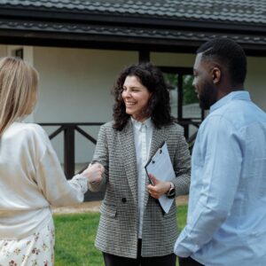 A real estate agent shakes hands with a couple outside a modern house, symbolizing a successful property deal.
